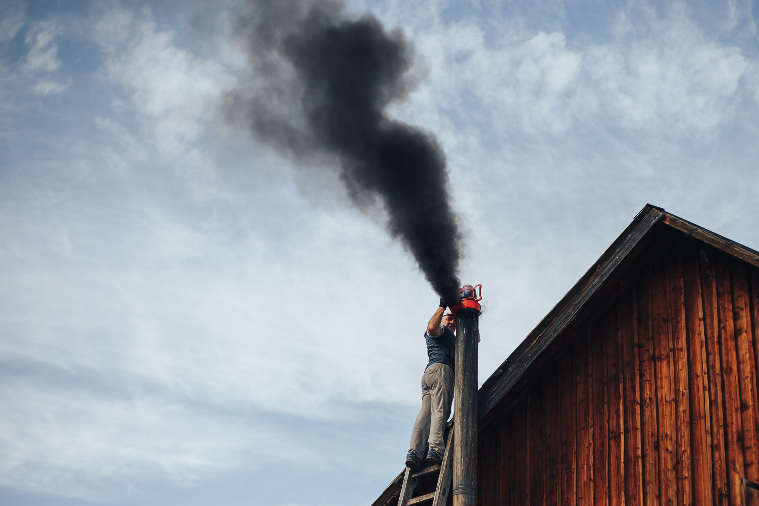 Chimney sweep in New York cleaning a residential chimney on a rooftop, showing risks of DIY chimney cleaning in Brooklyn, Queens, Manhattan, Bronx and Staten Island, with visible black smoke, highlighting the need for professional chimney sweep services in NYC homes and apartments.